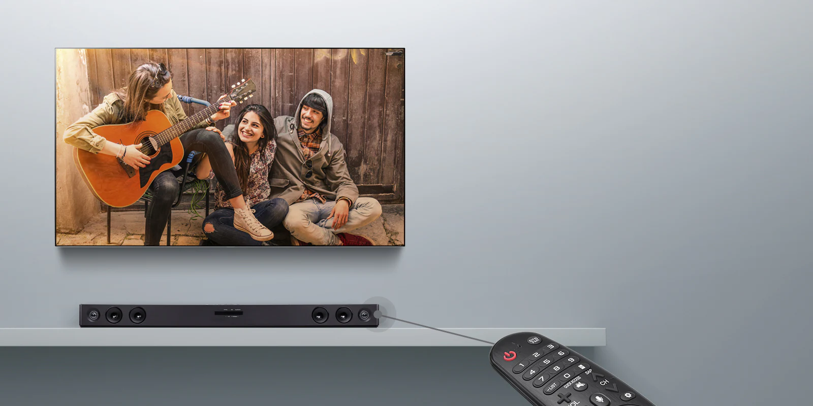 Закрепленный на серой стене телевизор LG, на экране которого демонстрируется фильм. Под ним находится саундбар LG. В правой части изображения показан пульт ДУ. Показана линия, соединяющая пульт с саундбаром, демонстрирующая, что пользователи могут управлять саундбаром с пульта ДУ.
