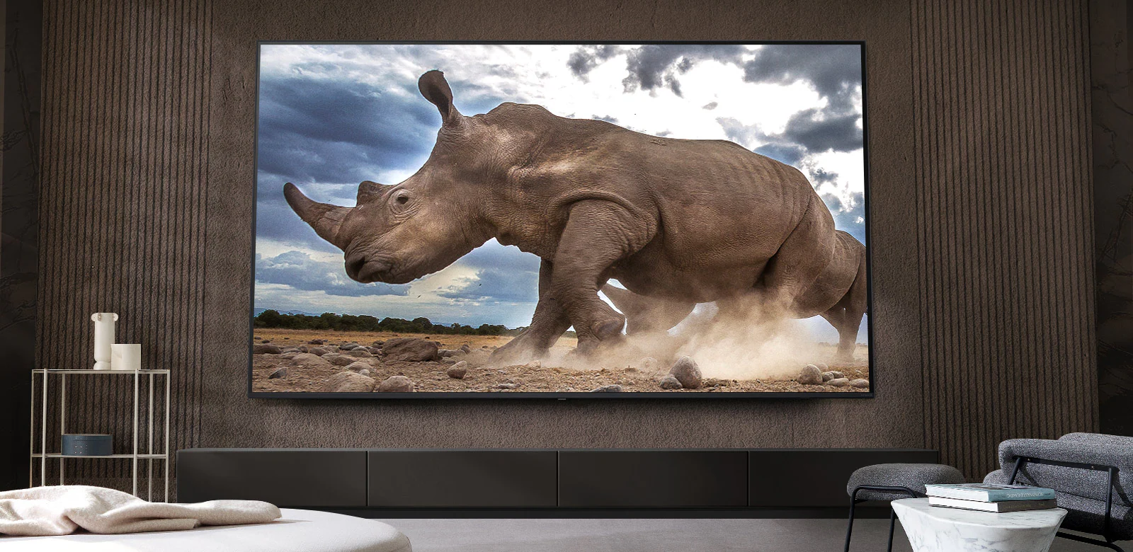 Носорог в обстановке сафари демонстрируется на сверхбольшом телевизоре LG&nbsp;TV, установленном на коричневой стене гостиной, окруженной модульной мебелью кремового цвета.